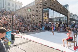 Zwei Artisten zeigen ihr Können auf dem Hauptbahnhof-Vorplatz am Döppersberg. Auf der Treppe sitzen zahlreiche Zuschauer.